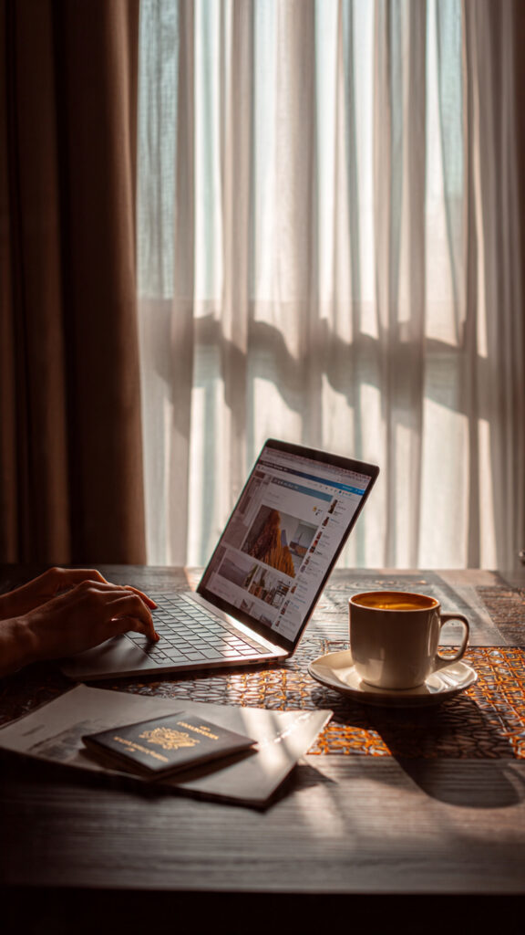  “Traveler using a laptop to search for cheap flights with a passport and coffee on the desk”