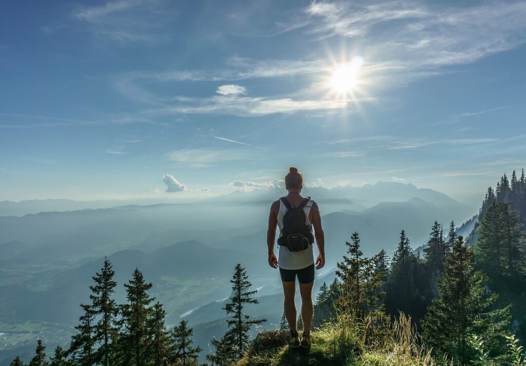 Traveler standing on a hill looking at a wide mountain landscape at sunset
