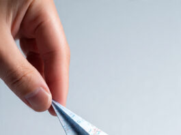 “Hand launching a paper airplane made from a ticket over a world map, symbolizing cheap and easy flight planning.”